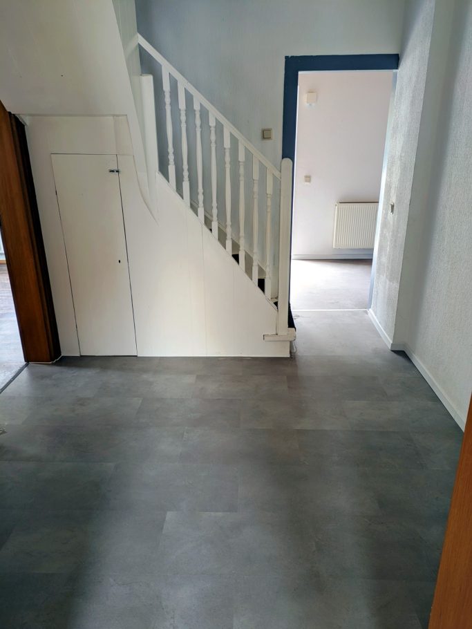 Bodenverlegung Heller Raum mit Treppe und offener Tür zu einem weiteren Raum.