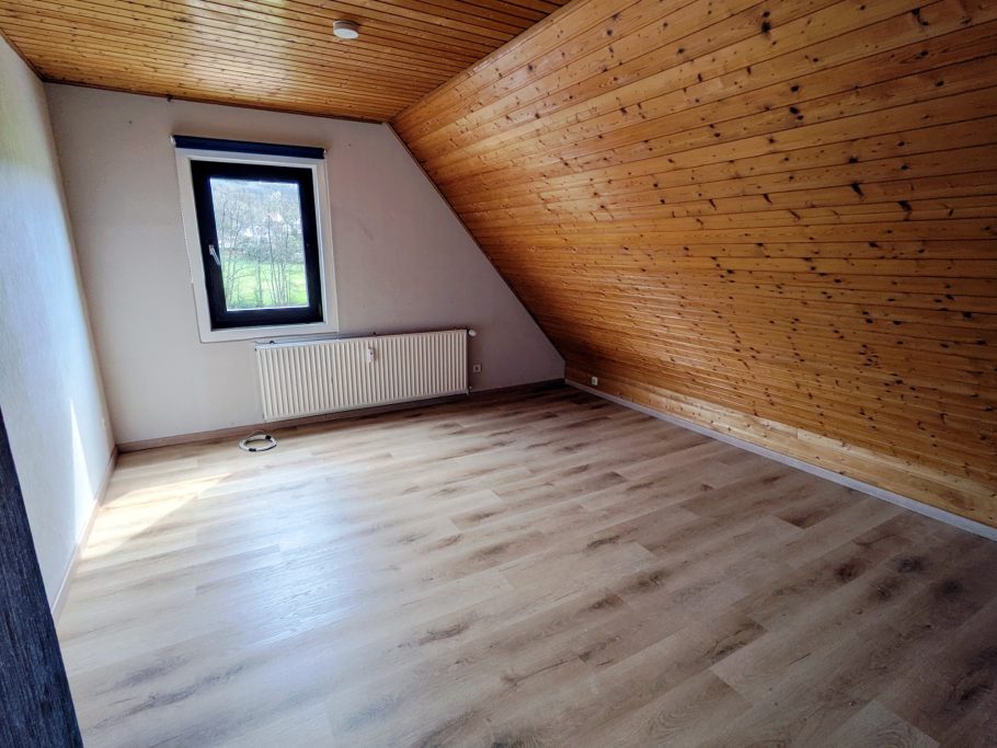 Bodenverlegung Räumlicher, unmöblierter Raum mit Holzdecke und Fenster. Helle Bodenfläche.