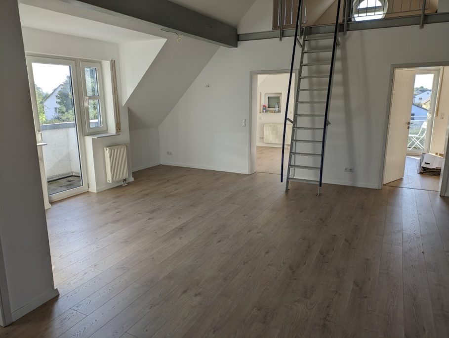 Bodenverlegung Geräumiger, lichtdurchfluteter Raum mit Holzfußboden und Zugang zu Balkontüren.