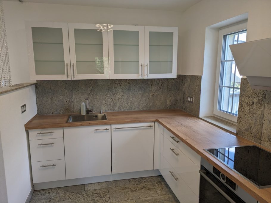 Küchenmontage Moderne Küche mit weißen Schränken, Holzarbeitsplatte und neuem Fenster.