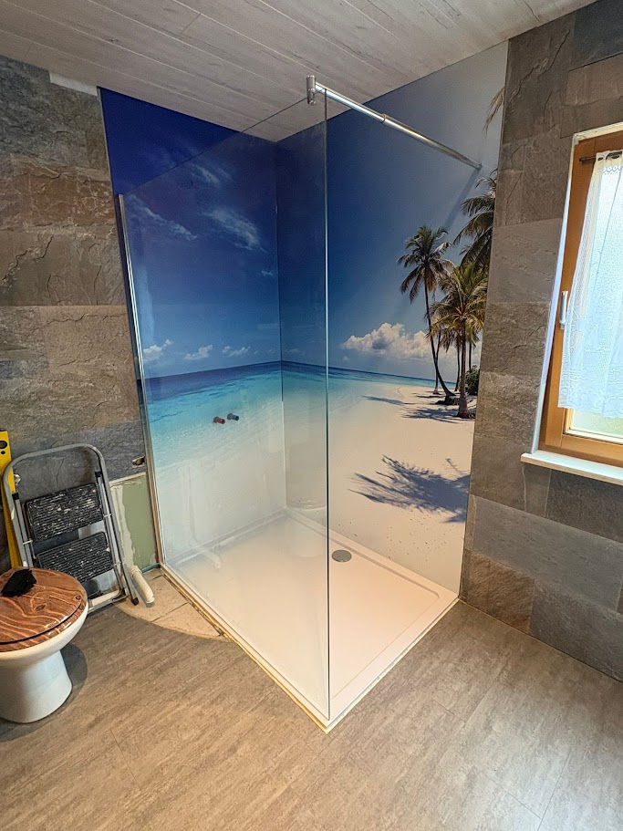 Montage ALU Verbundplatte Moderne Dusche mit Glasabtrennung und tropischem Strandmotiv an der Wand.